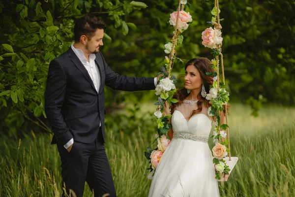 Beautiful bride with fiance is swinging on a swing — Stock Photo, Image