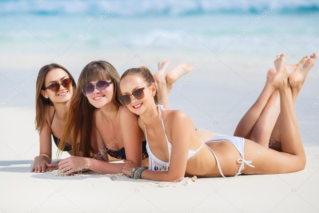 Three girls in bikini sunbathing lying on the sand of a tropical beach