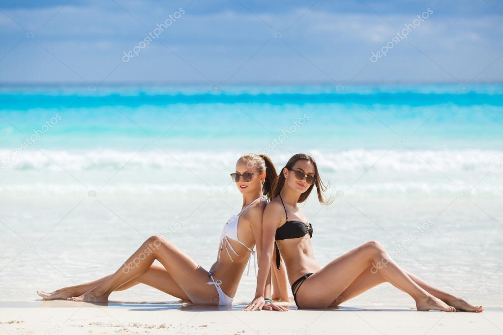 Girls in bikinis sunbathing, sitting on the beach