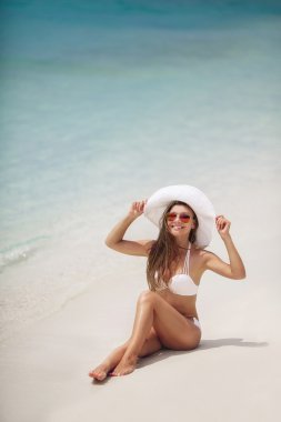 Bir beyaz bikini ve şapka tropikal bir plajda güzel kadın.
