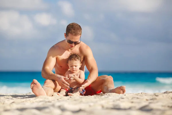 Padre joven con un hijo pequeño jugar cerca del océano . —  Fotos de Stock