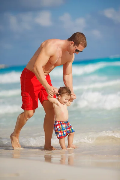 Padre joven con un hijo pequeño jugar cerca del océano . —  Fotos de Stock