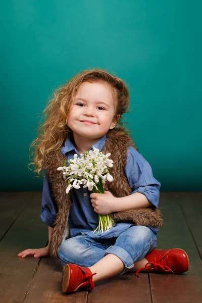Schönes kleines Mädchen mit einem großen Strauß Schneeglöckchen. — Stockfoto