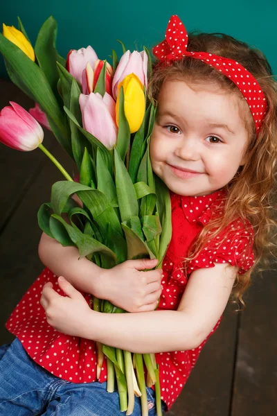 Beautiful little girl with a big bouquet of tulips. — Stock Photo, Image