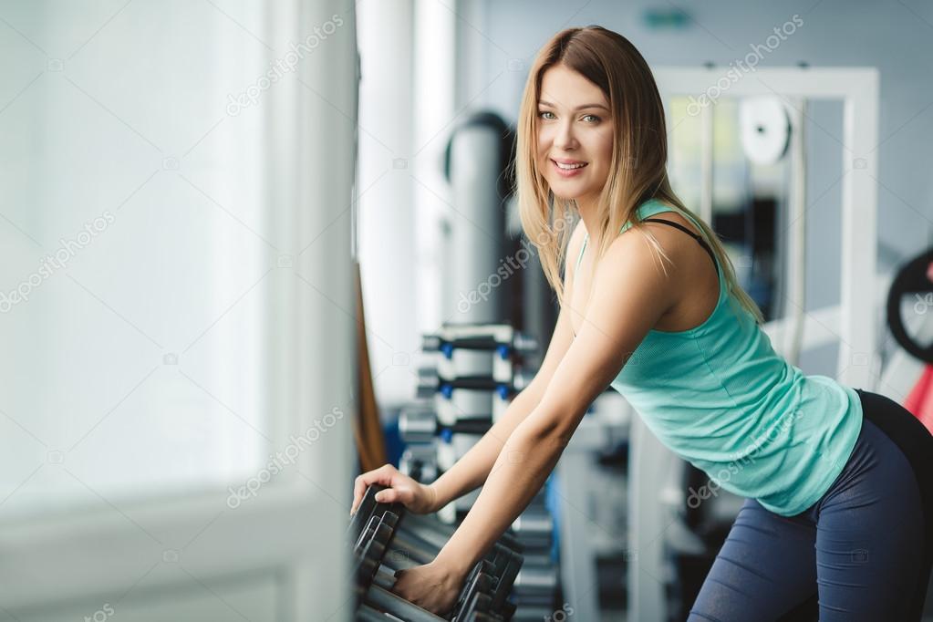 Beautiful girl fitness trainer chooses dumbbells for training.