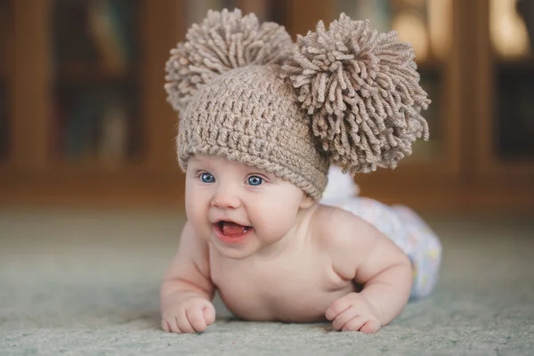 The newborn girl in a hat, lying on the floor, looking up. — Stock Photo, Image