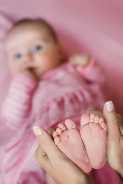 Bir şefkatle küçük bir bebeğin bacakları tutan anne bakım eller. — Stok fotoğraf