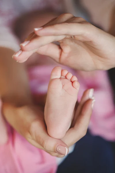 Caring hands of mother tenderly holding a tiny baby's legs. — Stock Photo, Image