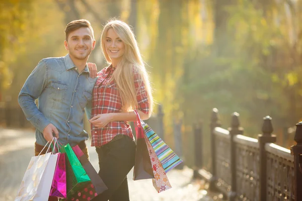 Feliz pareja joven con una bolsa de papel en un parque en otoño . — Foto de Stock