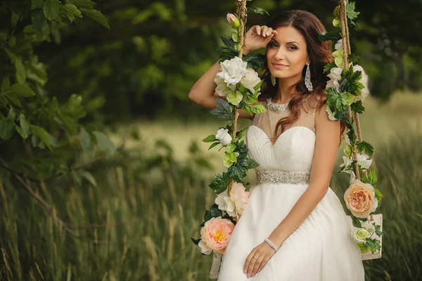 Schöne Braut, die auf einer Schaukel schwingt, die mit Blumen geschmückt ist. — Stockfoto
