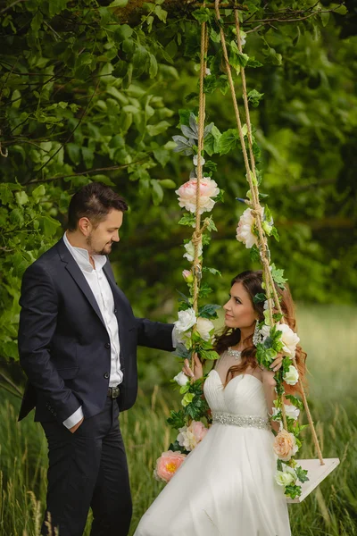 Lo sposo fa oscillare la sposa su un'oscillazione in parco all'aperto — Foto Stock
