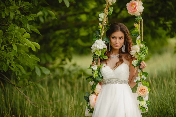 Όμορφη νύφη ταλαντώσεις σε μια κούνια που είναι διακοσμημένα με λουλούδια. — Φωτογραφία Αρχείου