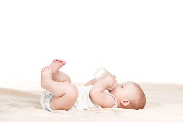 Cute baby with a bottle of milk on a beige blanket — Stock Photo, Image