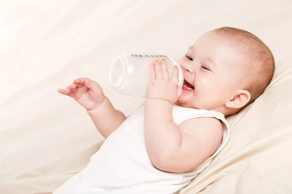 Cute baby with a bottle of milk on a beige blanket — Stock Photo, Image