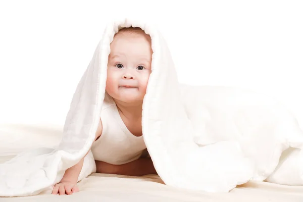 Χαριτωμένο μωρό κρυφοκοιτάζουν έξω από κάτω από το κάλυμμα, που παίζει στο κρεβάτι. — Φωτογραφία Αρχείου