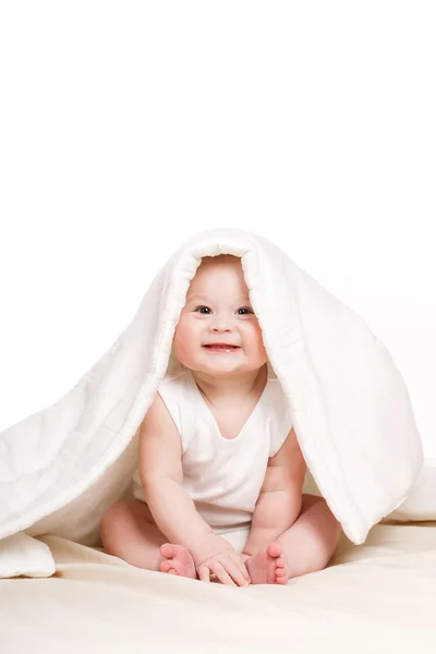 Bebê bonito espreitando debaixo do cobertor, brincando na cama . — Fotografia de Stock