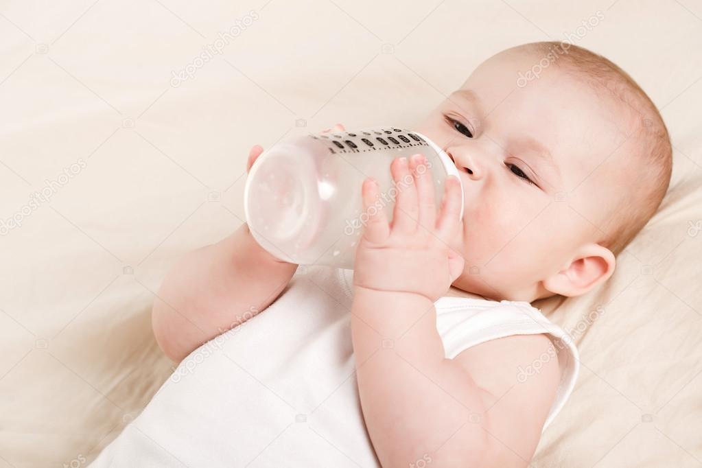 Cute baby with a bottle of milk on a beige blanket