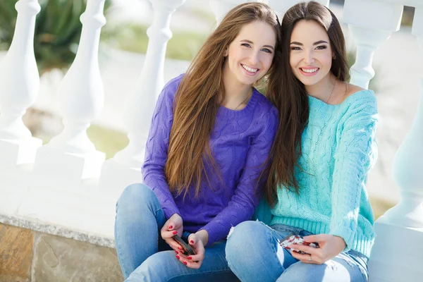 Two beautiful girlfriends watching pictures and listening to music on their smartphones. — Stock Photo, Image