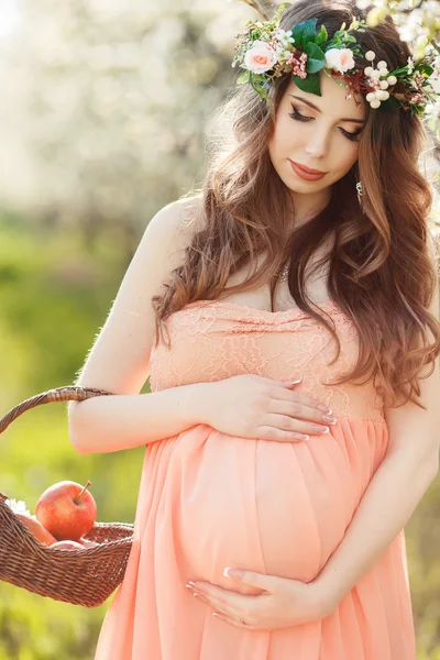Mulher grávida no jardim da primavera com uma cesta de maçãs maduras . — Fotografia de Stock