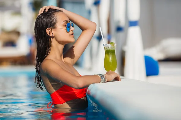 Elegante jonge vrouw in het zwembad met een cocktail. — Stockfoto