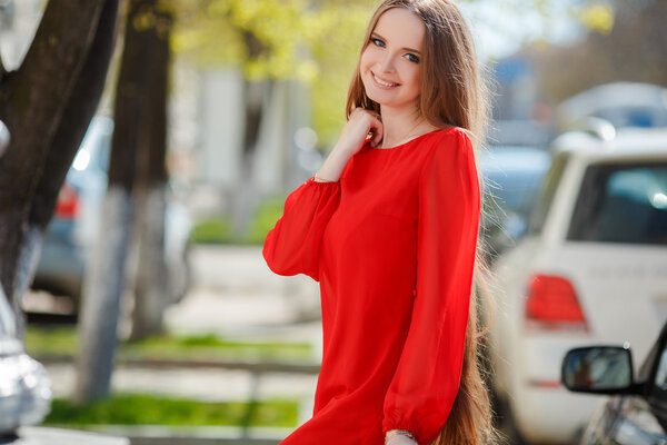 Молодая красивая женщина стоит на городской улице с новой машиной на заднем плане
