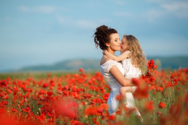 Mother with her little daughter in her arms in a field of blooming poppies.