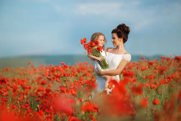 Madre con su hijita en brazos en un campo de amapolas florecientes . — Foto de Stock