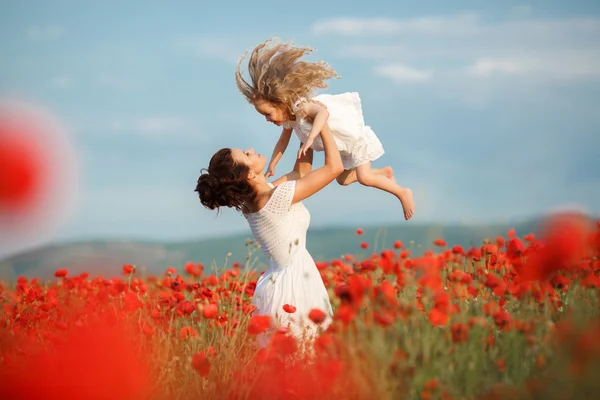 Mère avec sa petite fille dans les bras dans un champ de coquelicots en fleurs . — Photo