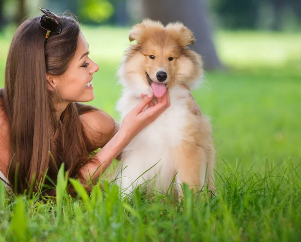 Jovem mulher bonita jogando em um parque verde com um pequeno filhote de cachorro collie — Fotografia de Stock
