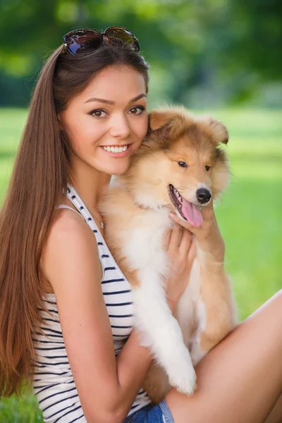 Jovem mulher bonita jogando em um parque verde com um pequeno filhote de cachorro collie — Fotografia de Stock