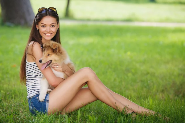 Jovem mulher bonita jogando em um parque verde com um pequeno filhote de cachorro collie — Fotografia de Stock