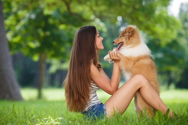 Joven hermosa mujer jugando en un parque verde con un pequeño cachorro collie — Foto de Stock