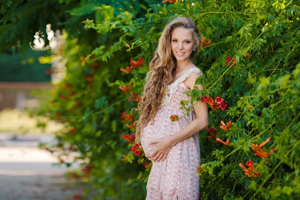 Красивая беременная женщина рядом с цветущим кустом в парке — стоковое фото