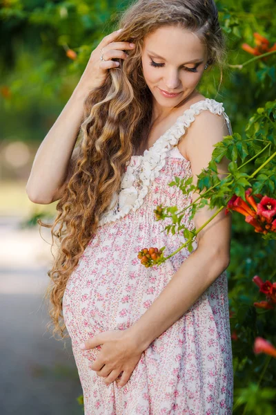 Beautiful pregnant woman near the blossoming bush in the park — Stock Photo, Image