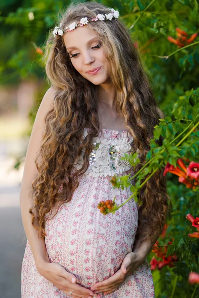 Krásná těhotná žena poblíž kvetoucí bush v parku — Stock fotografie