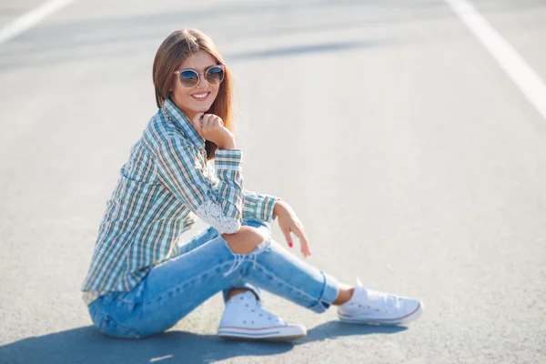 Cheerful beautiful woman smiling sitting on the road — Stock fotografie