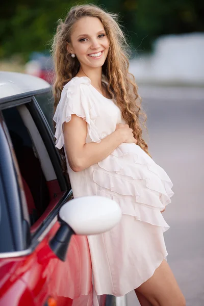 Těhotná brunetka a její červené auto — Stock fotografie