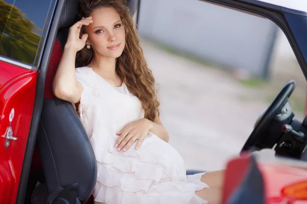 Schwangere Brünette und ihr rotes Auto — Stockfoto