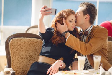 Young couple watching photos on mobile phone, sitting in a caf