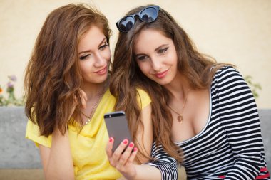 Two happy girlfriends view photos on a mobile phone