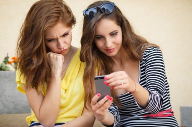 Two happy girlfriends view photos on a mobile phone