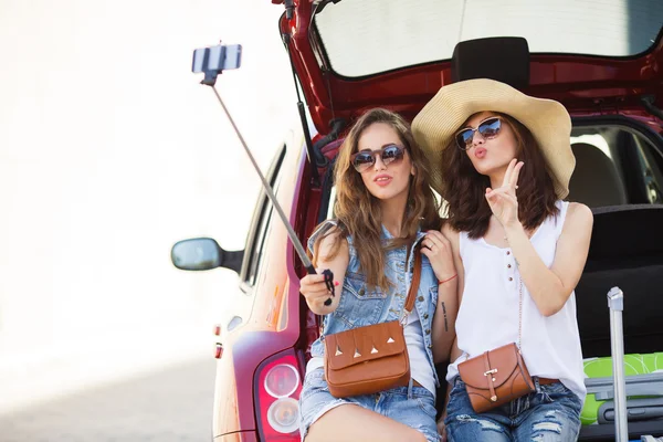 Two female friends talking while sitting in the open trunk of a car — Stock Photo, Image