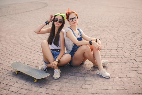 Two beautiful young girls on a skateboard in the city. — Stock Photo, Image