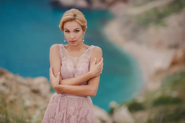 Sposa in abito da sposa si erge su una scogliera con una splendida vista sul mare dalla cima — Foto Stock