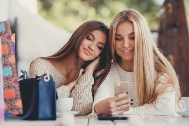 Two young women at cafe looking at pictures of new gadgets