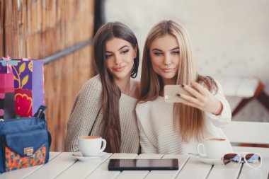 Two young women at cafe looking at pictures of new gadgets