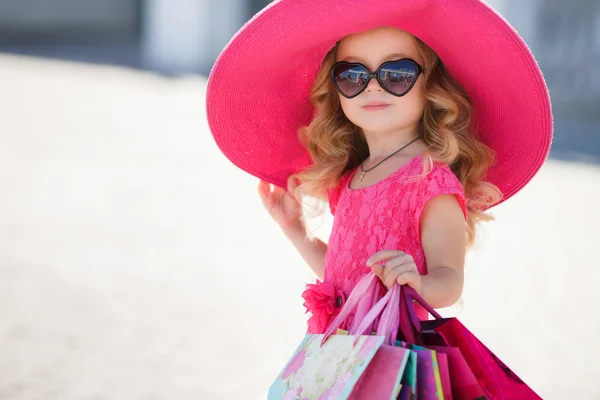 Fashionable little girl in a hat with shopping bags