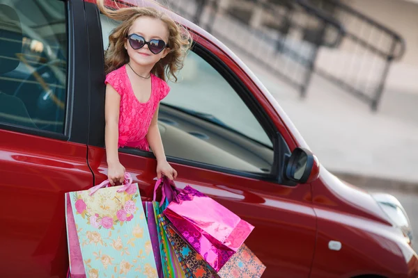 Happy child in the car with colored bags — Stockfoto