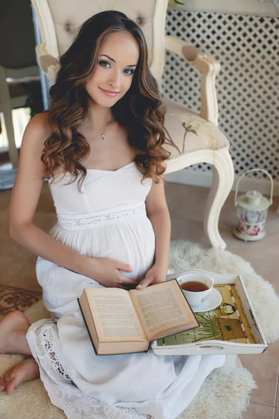 Mulher grávida lendo um livro sentado no chão — Fotografia de Stock