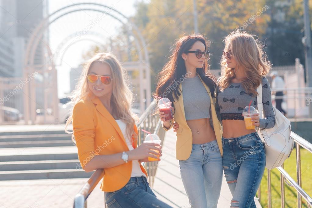 Three girls are walking in the Park in summer and drink fruit juice